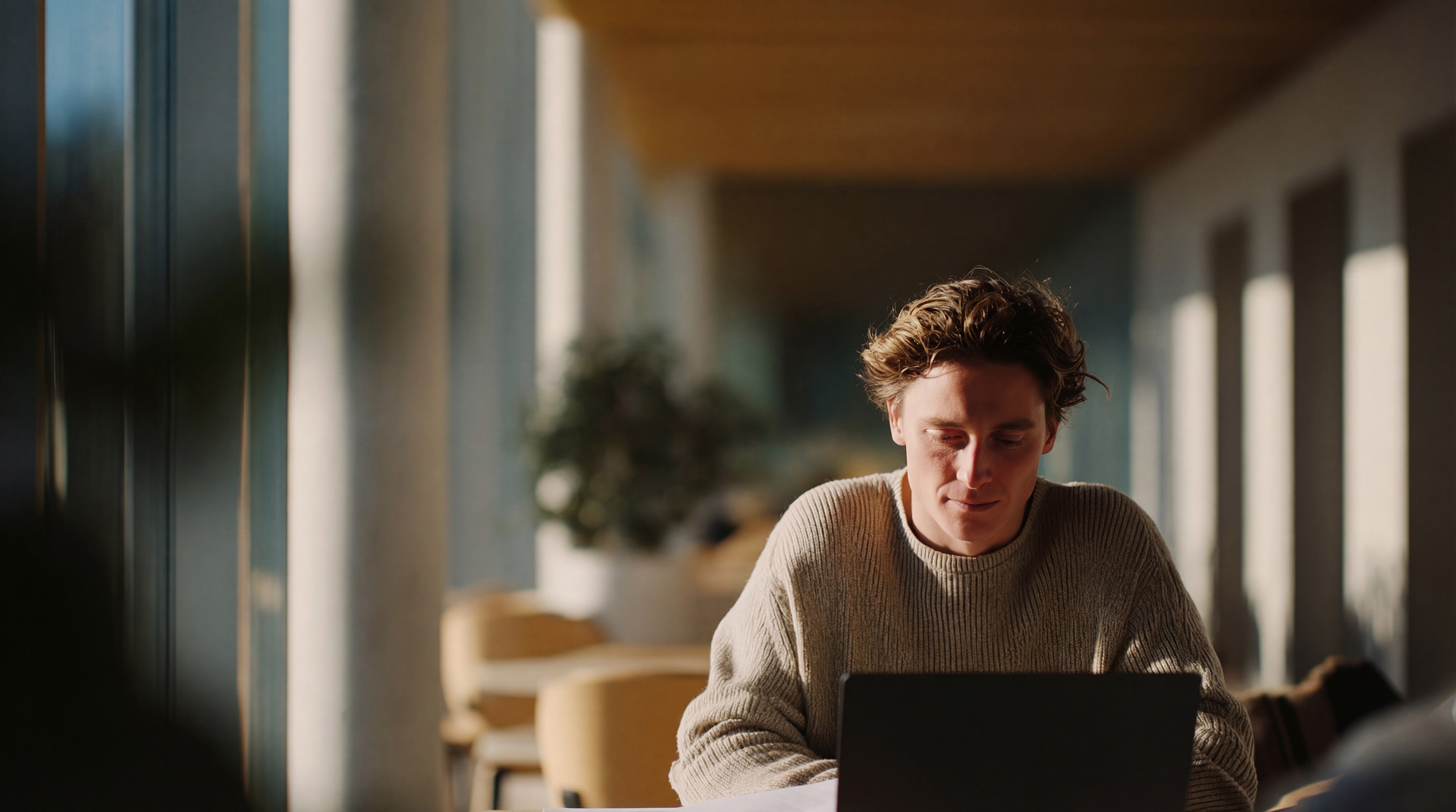 Säljare vid laptop i morgonljus på ett skandinaviskt kontor